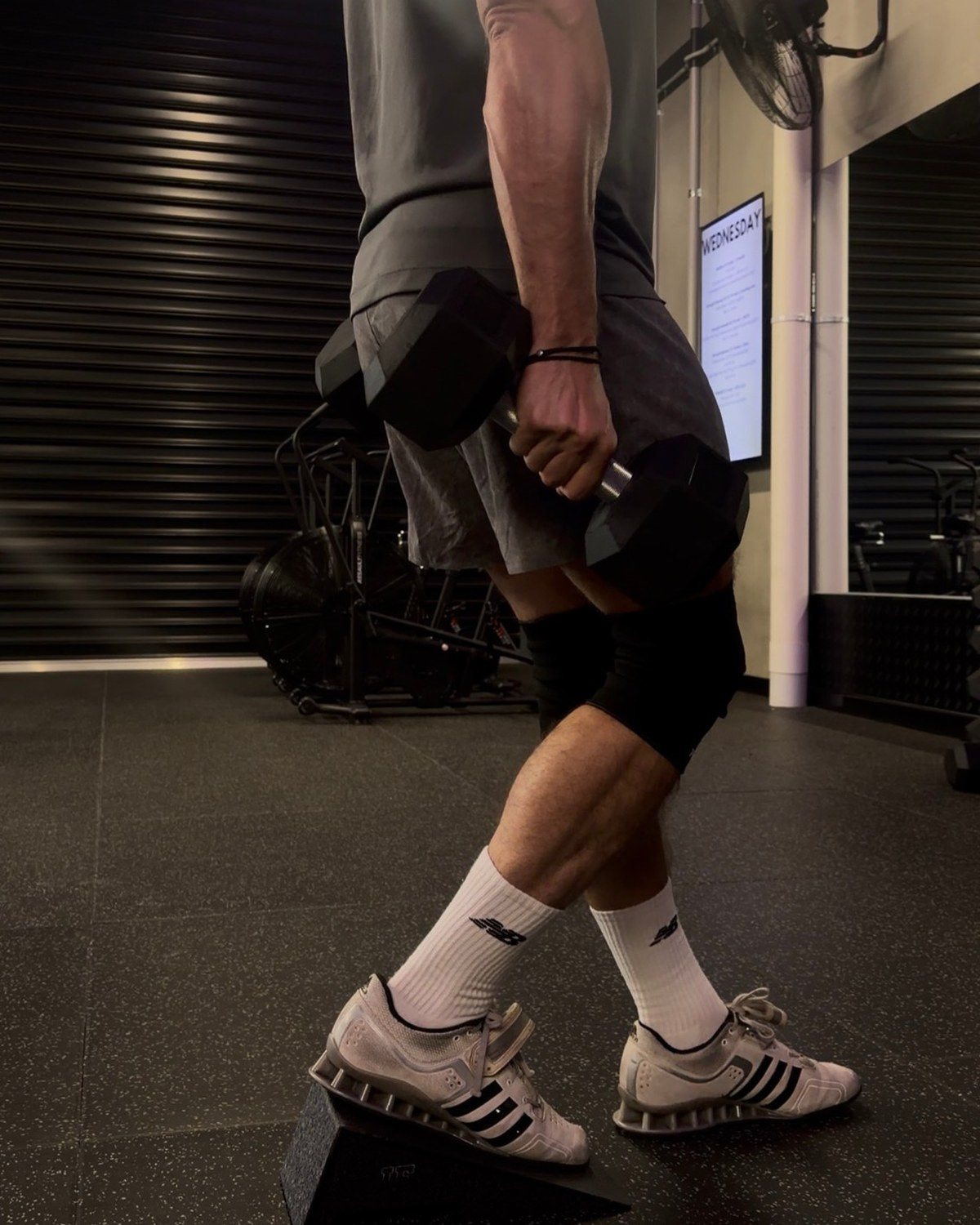 A Poliquin step down with the heel raised on a slant wedge, holding a dumbbell